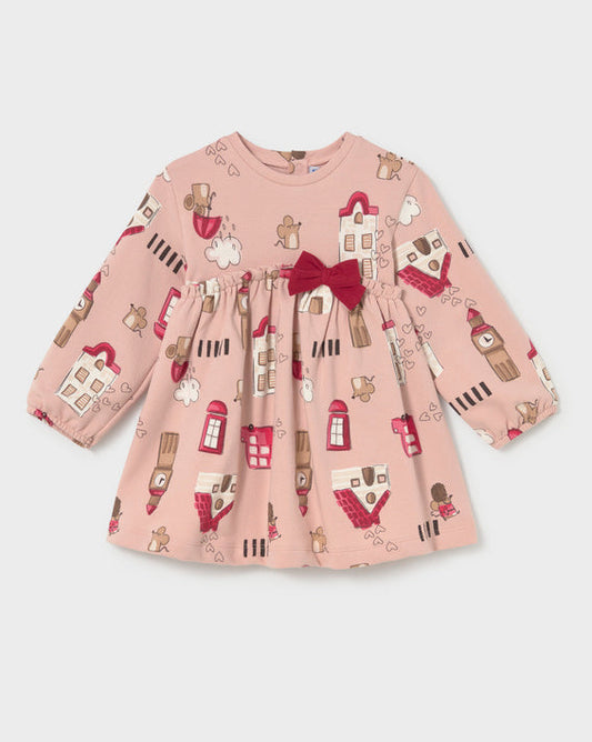 A long-sleeve baby dress in dusty pink with an all-over London-themed print of red buses, tea time phones, and houses, featuring a dark red bow at the waist.