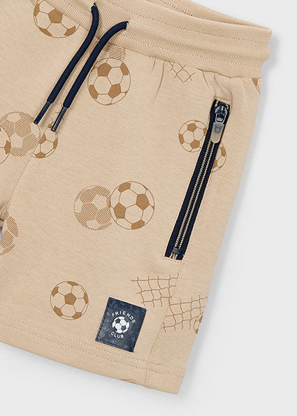 Beige shorts with soccer ball pattern and zipper on a tan background