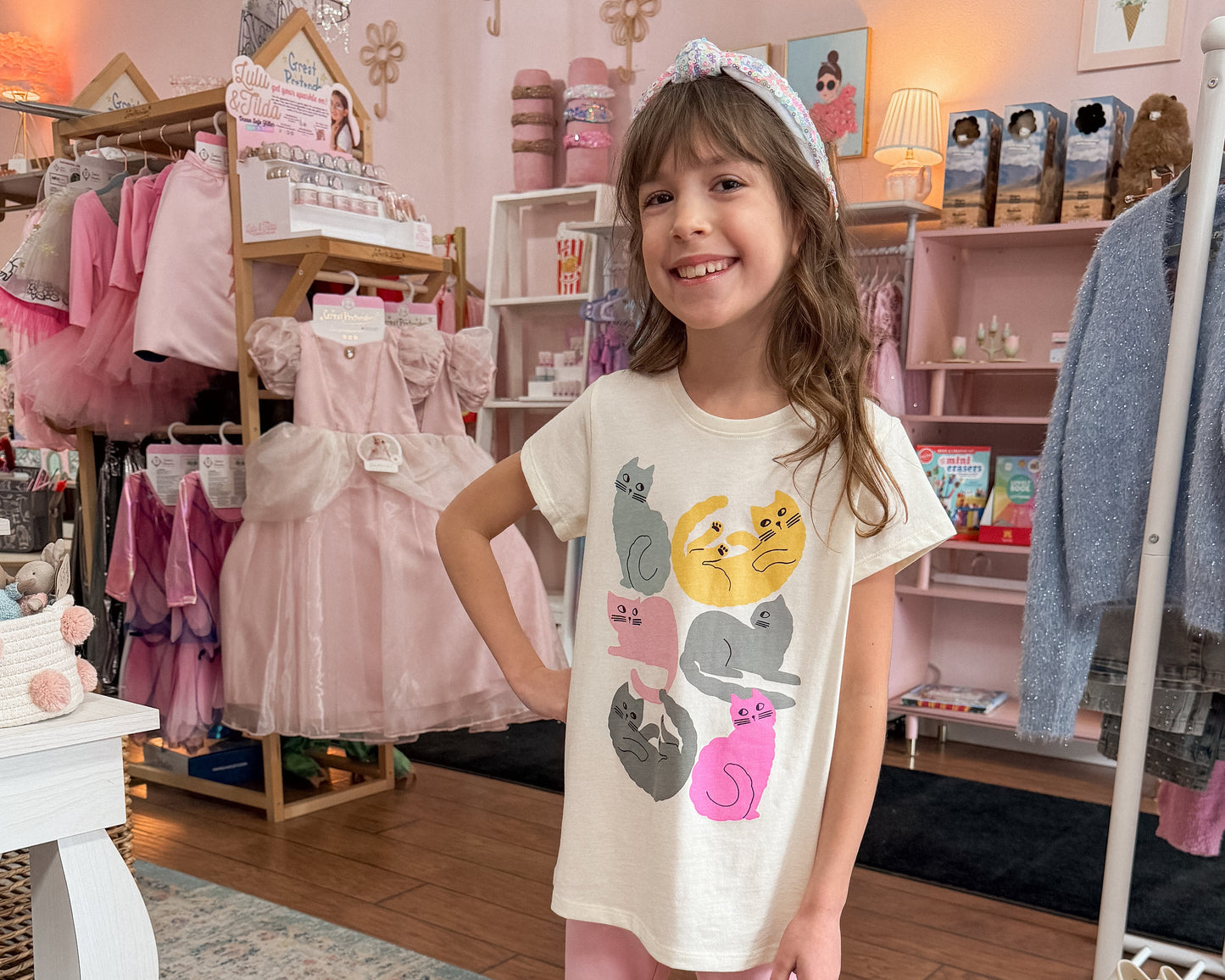 Young girl in a store wearing a white t-shirt with cartoon designs and pink pants.