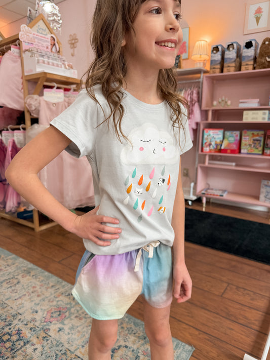 Young girl wearing a white t-shirt with colorful designs and pastel shorts in a store setting.