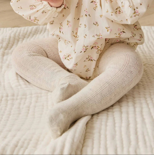 Baby sitting on a bed wearing a floral outfit with a neutral background