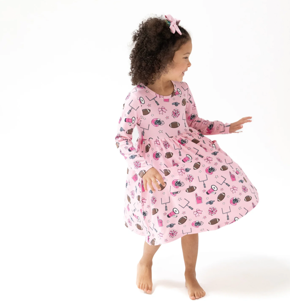 Child wearing a pink dress with football themed print on a white background