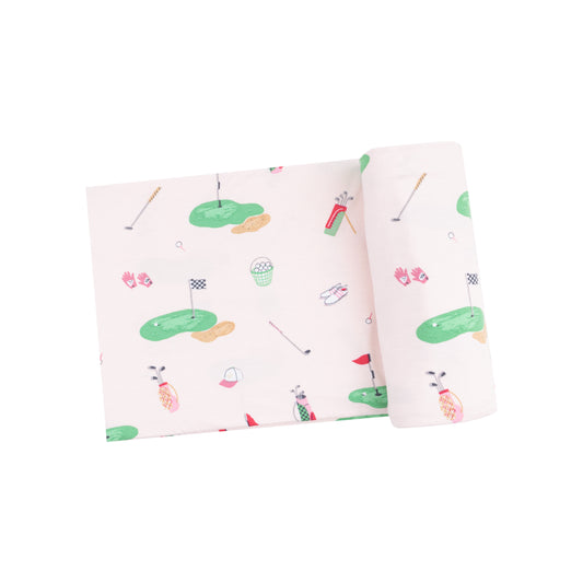 A folded pink swaddle blanket with a golf-themed pattern including illustrations of golf balls, tees, and holes.