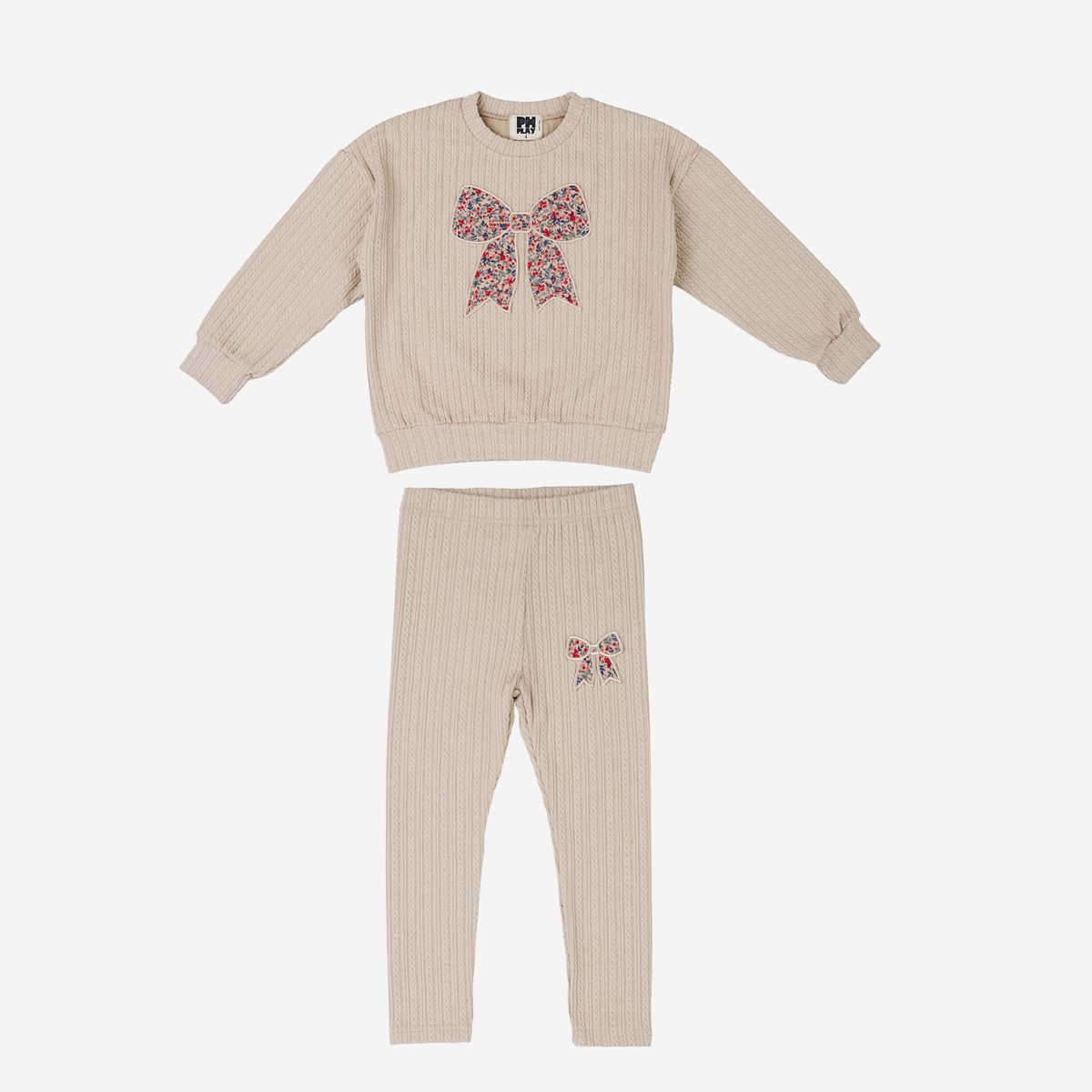 A two-piece children's ribbed knit pajama set in beige, featuring a long-sleeve top with a large multicolor bow graphic on the chest and matching pants with a smaller bow graphic on the upper thigh.
