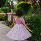 Child in a pink top and floral skirt standing in a garden.