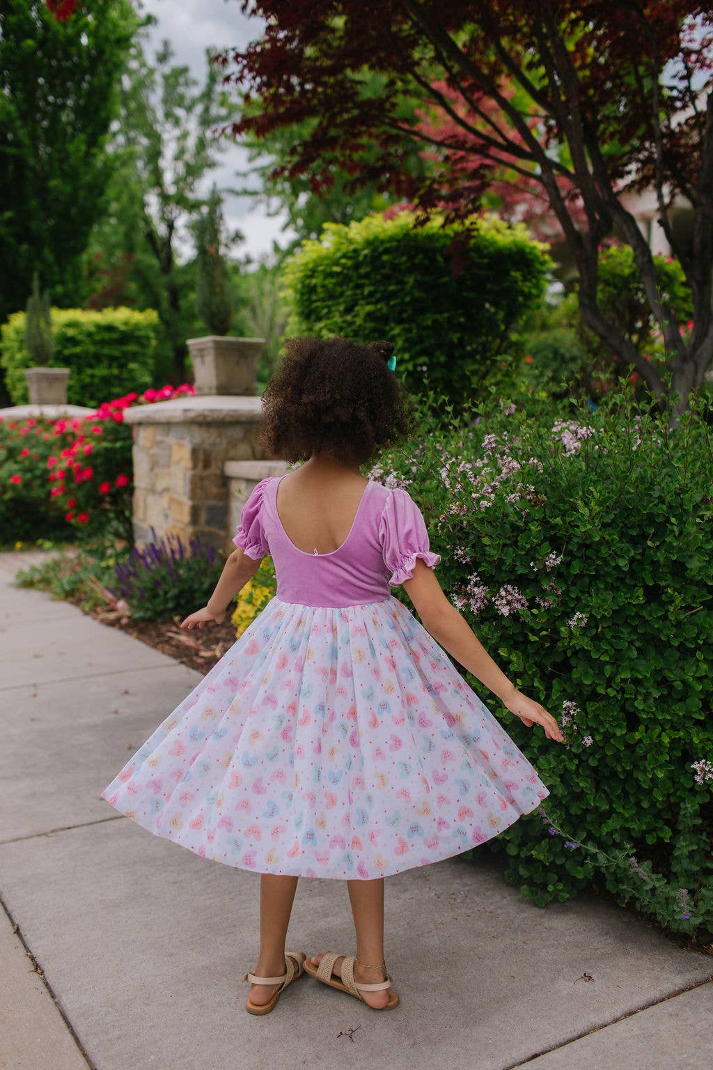 Child in a pink top and floral skirt standing in a garden.