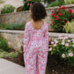 Person wearing a pink floral jumpsuit standing in a garden with flowers and a stone wall.