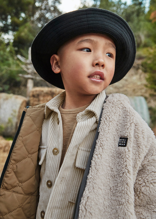 Child wearing a black hat and layered clothing outdoors