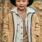 Child wearing a beige quilted jacket and black hat outdoors