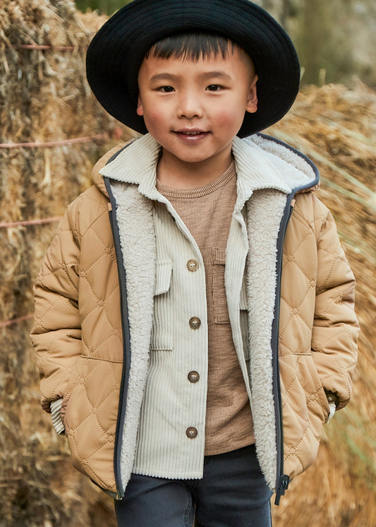 Child wearing a beige quilted jacket and black hat outdoors