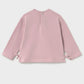 A dusty pink long-sleeve top shown from the back, featuring a simple crew neck and side tie details at the cuffs, photographed against a light gray background.