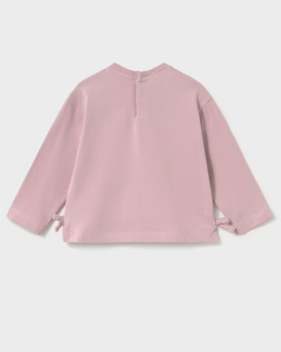 A dusty pink long-sleeve top shown from the back, featuring a simple crew neck and side tie details at the cuffs, photographed against a light gray background.