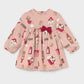 A long-sleeve baby dress in dusty pink with an all-over London-themed print of red buses, tea time phones, and houses, featuring a dark red bow at the waist.
