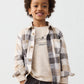 Child wearing a plaid shirt over a graphic t-shirt with a plain background