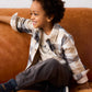 Child sitting on a brown couch wearing a plaid shirt and gray pants.