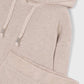 Close-up of a ribbed knit hoodie in a light warm beige or blush-taupe color, showing the hood, braided drawstrings, and part of a matching ribbed garment or folded section at the bottom. A small interior neck label is visible.
