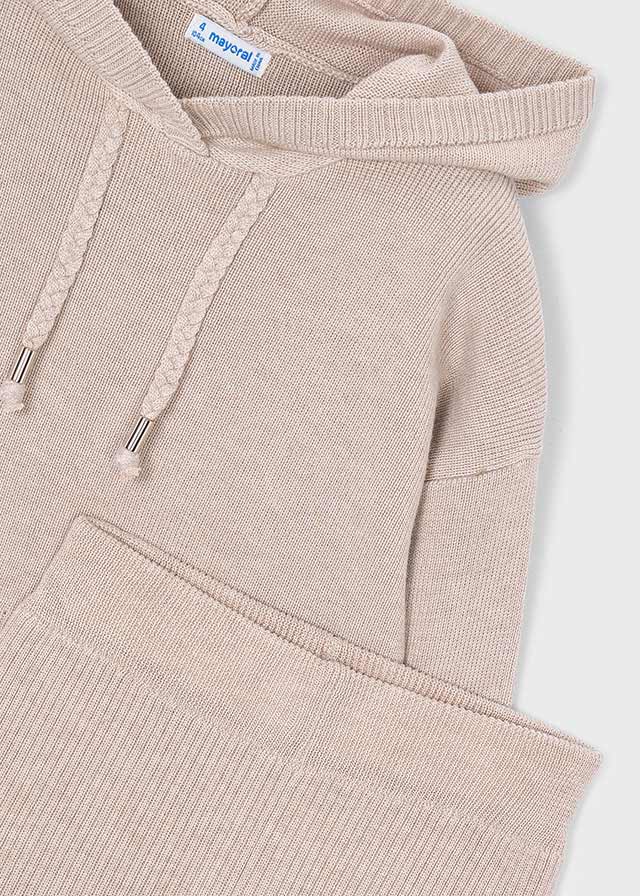 Close-up of a ribbed knit hoodie in a light warm beige or blush-taupe color, showing the hood, braided drawstrings, and part of a matching ribbed garment or folded section at the bottom. A small interior neck label is visible.