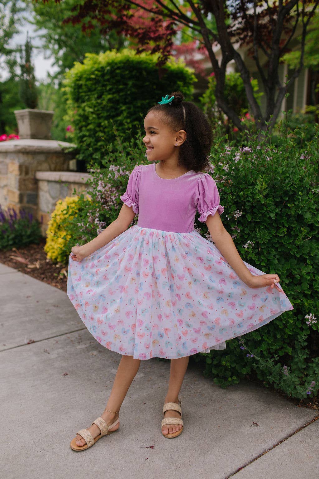Young girl in a pink and floral dress standing outdoors with greenery in the background