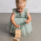 Child in a light green dress playing with wooden blocks on a plain background