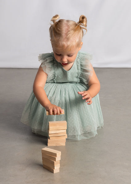 Child in a light green dress playing with wooden blocks on a plain background
