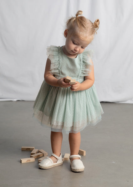 Young girl in a light green dress standing on a gray floor with wooden blocks.