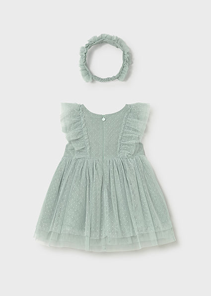Green baby dress with ruffled details and matching headband on a light gray background