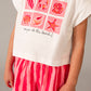 Child wearing a white t-shirt with pink sea-themed graphics and red striped shorts on a gray background