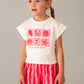 Young girl wearing a white t-shirt with pink graphics and red striped shorts on a gray background
