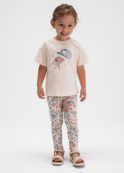 Child wearing a light pink t-shirt with a design and floral leggings on a white background