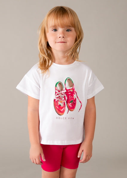Child wearing a white t-shirt with red shoes and 'Dolce Vita' text on a plain background