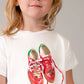 Child wearing a white t-shirt with red shoes and 'Dolce Vita' text