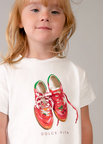 Child wearing a white t-shirt with red shoes and 'Dolce Vita' text