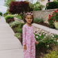 Young girl in a floral dress standing on a sidewalk with garden and house in the background