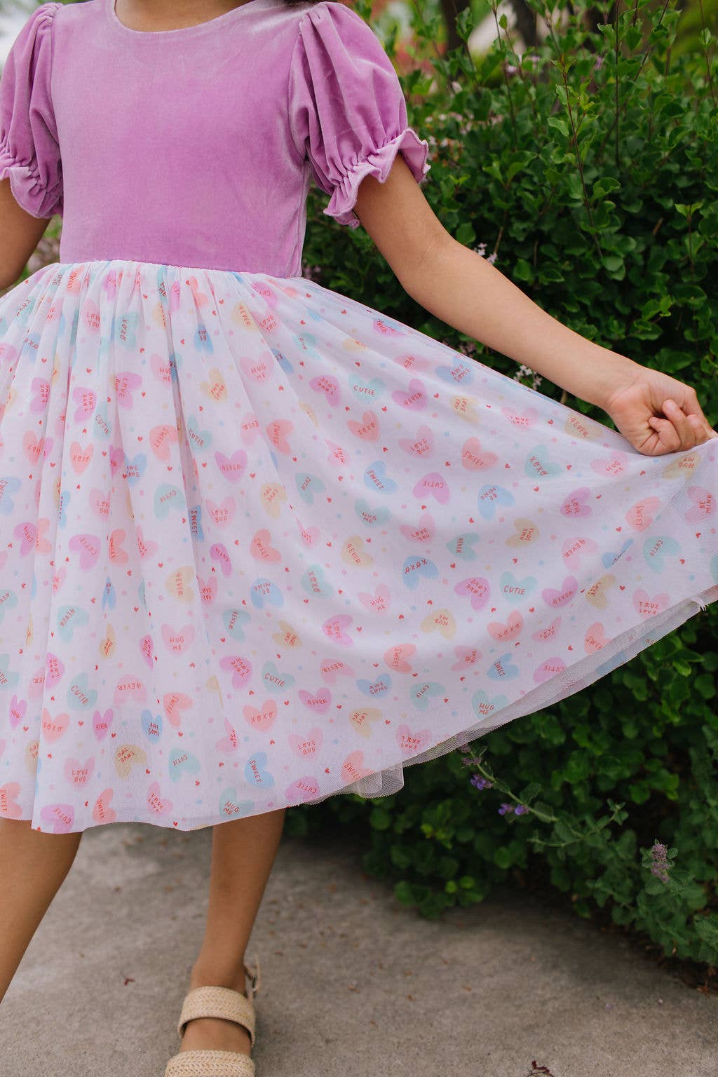 Child wearing a pink top and floral skirt with greenery in the background