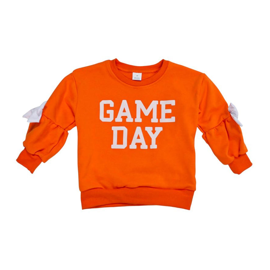 An orange crewneck sweatshirt with 'GAME DAY' printed in white block letters on the front, featuring white bow details on the sleeves, shown against a plain white background.