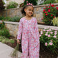 Young girl in a floral outfit standing outdoors with flowers and a garden in the background