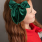 Child wearing a green bow headband against a gray background
