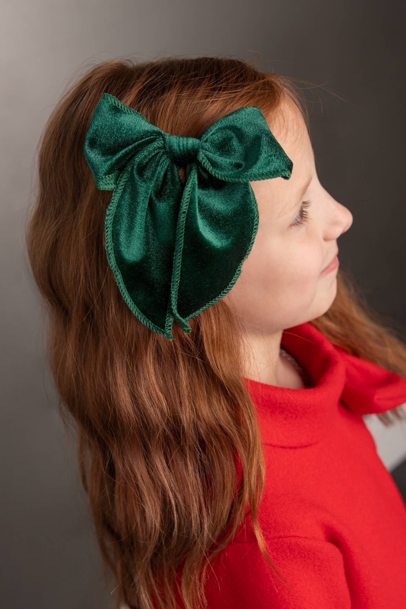 Child wearing a green bow headband against a gray background