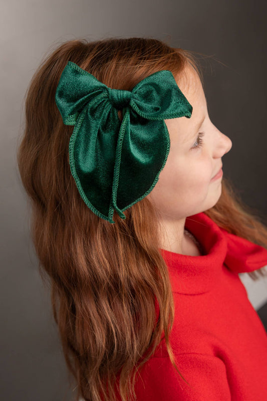Child wearing a green bow headband against a gray background