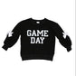 A black long-sleeve sweatshirt with 'GAME DAY' printed in bold white block letters across the chest, featuring white bow details on the sleeves, shown against a plain white background.