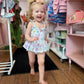 Child in a patterned outfit standing in a store with shelves and clothing in the background