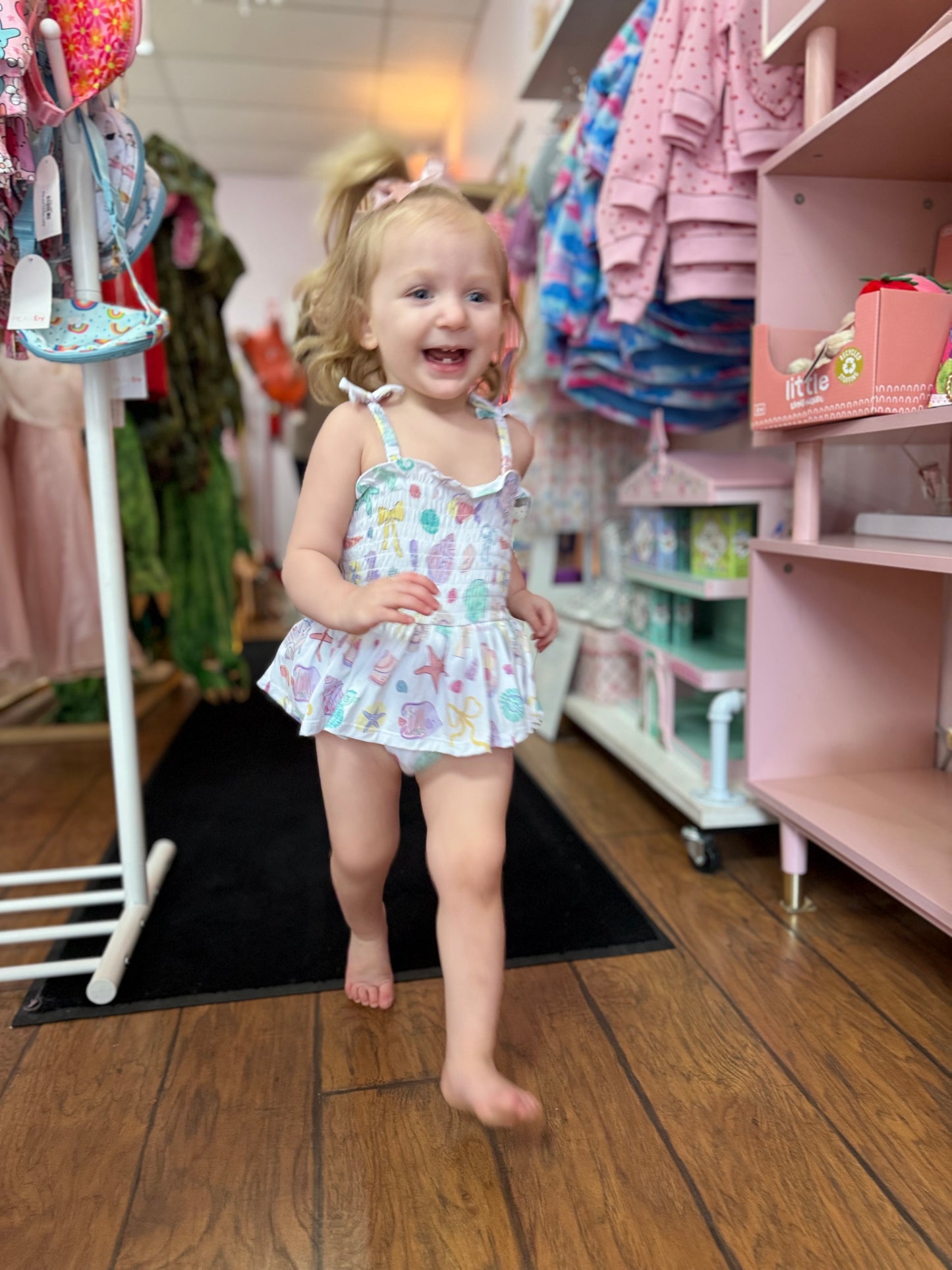 Child in a patterned outfit standing in a store with shelves and clothing in the background