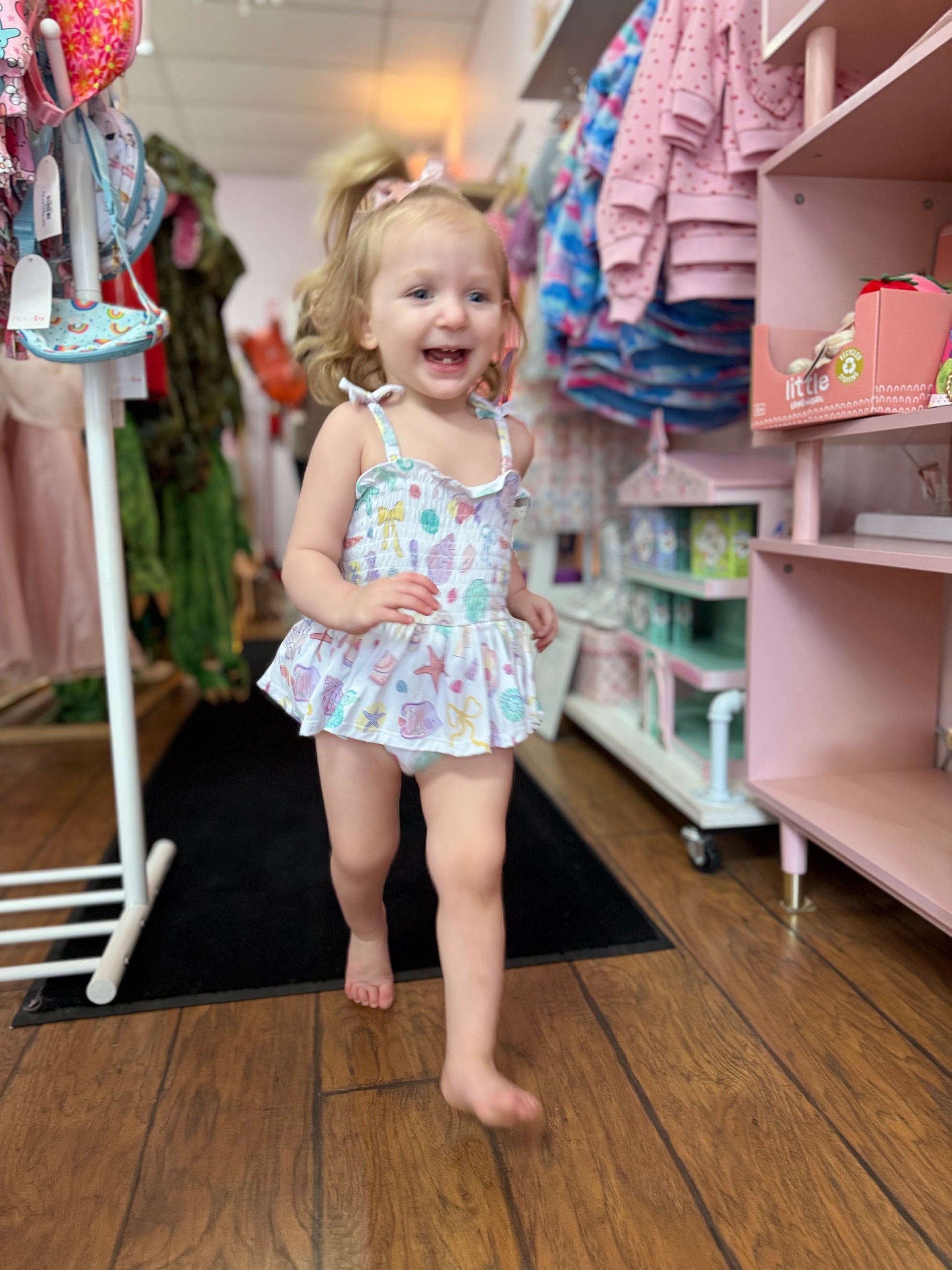Child in a patterned outfit standing in a store with shelves and clothing in the background