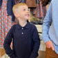 Young boy in a navy long-sleeve shirt with a collar standing next to a taller boy  in a clothing store.