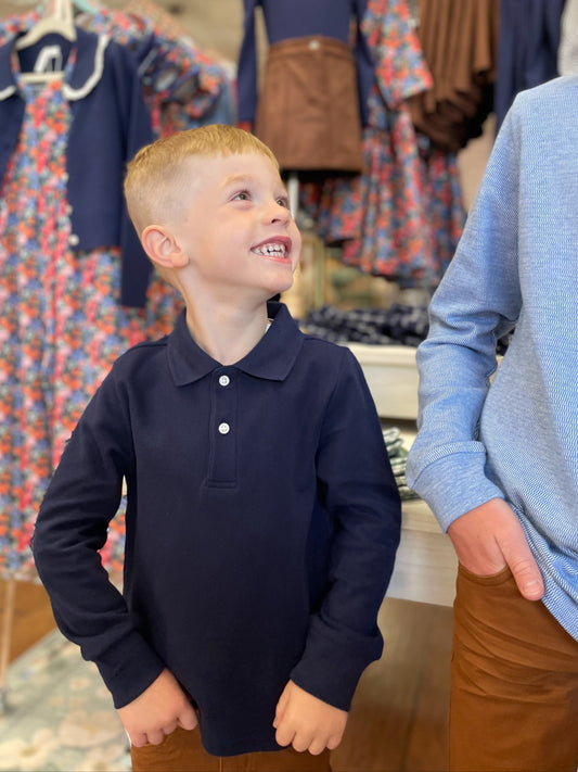 Young boy in a navy long-sleeve shirt with a collar standing next to a taller boy  in a clothing store.