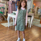 Young girl in a green dress and pink sweater standing in a clothing store.