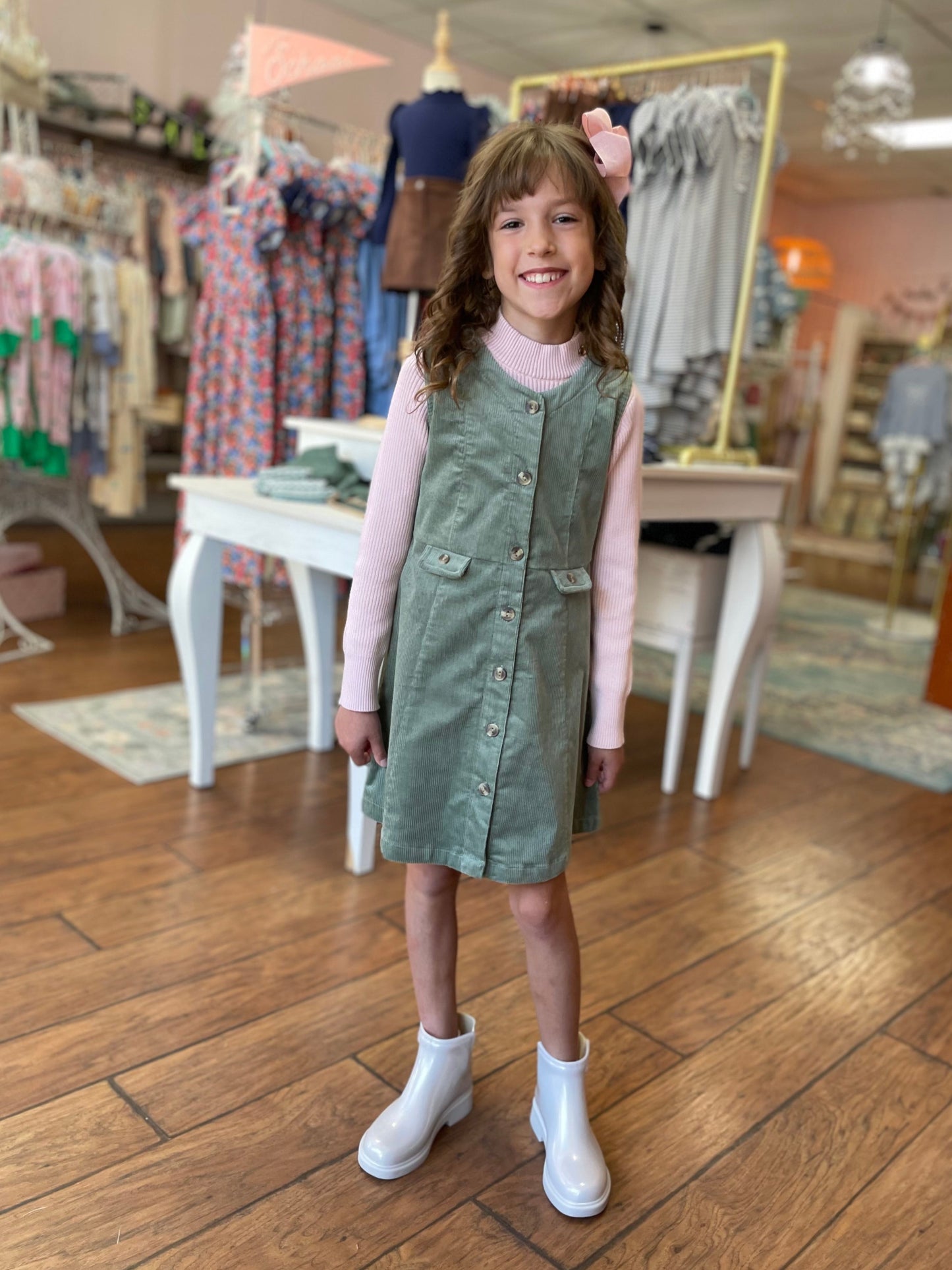 Young girl in a green dress and pink sweater standing in a clothing store.