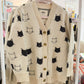 Beige cardigan with black cat pattern on a rack in a store setting