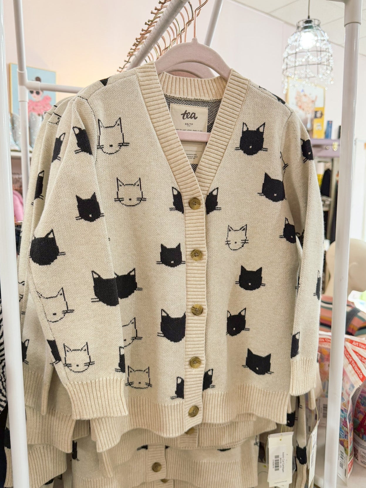 Beige cardigan with black cat pattern on a rack in a store setting