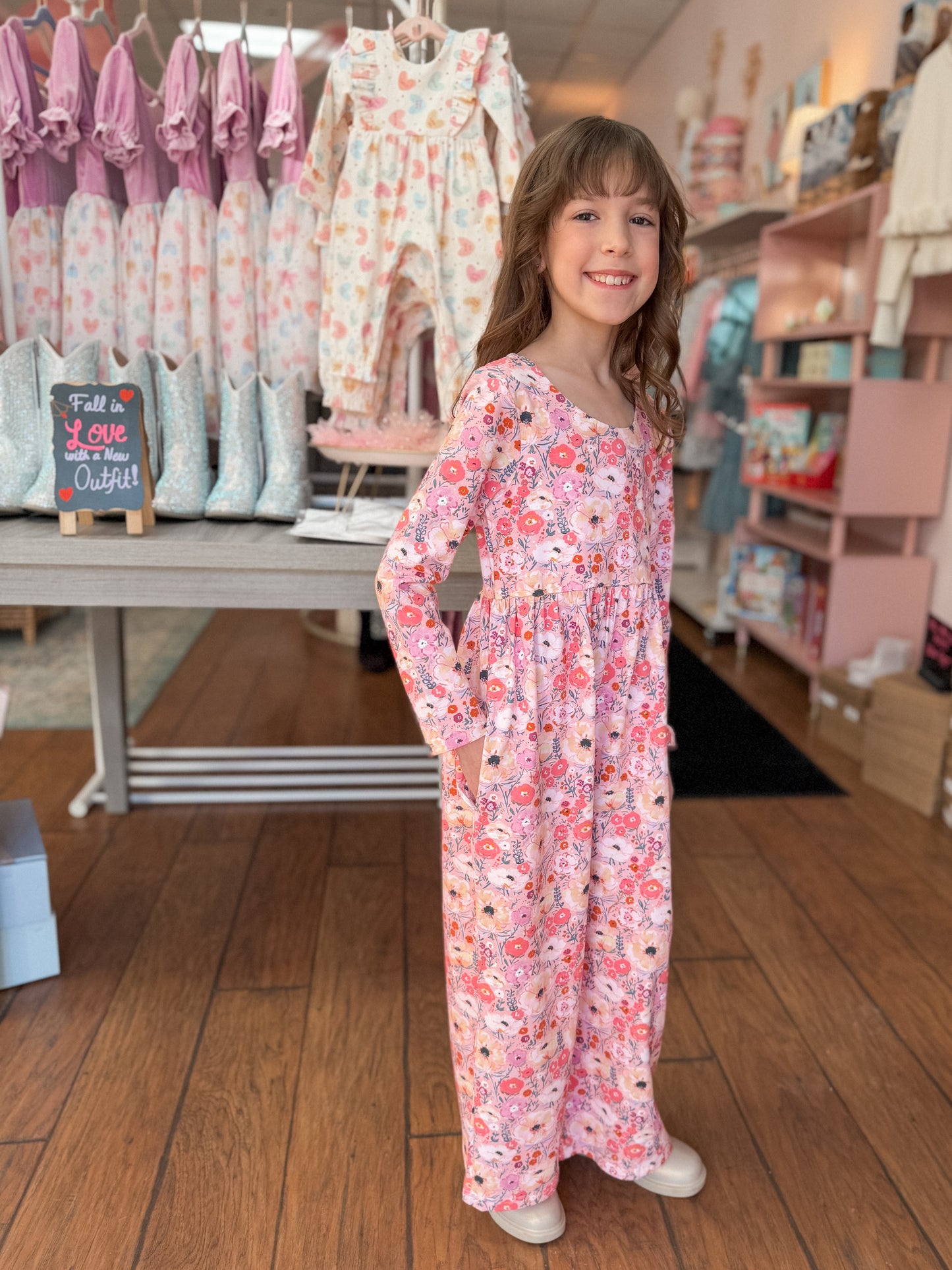 Young girl in a floral romper standing in a store with clothing and shoes in the background.